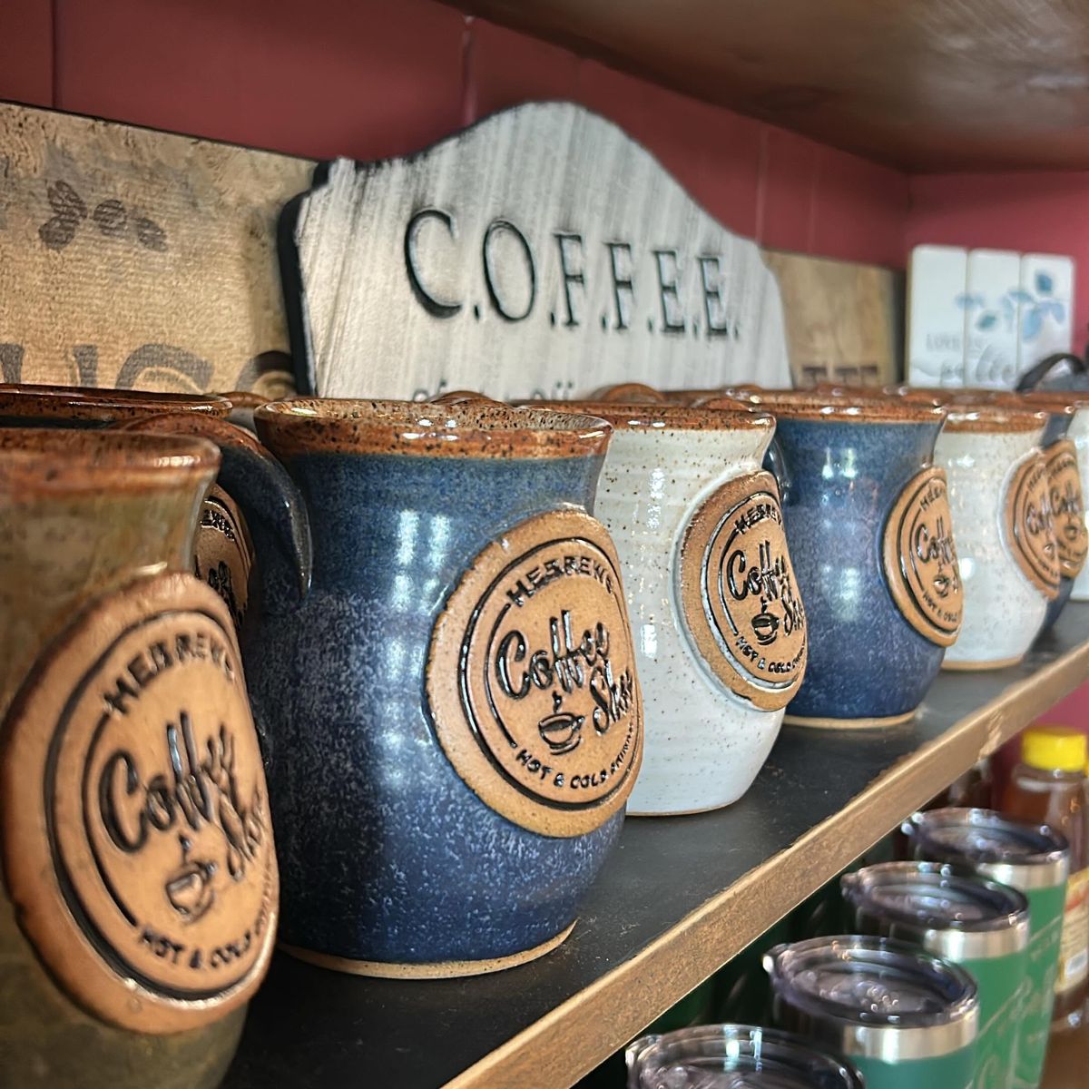 Handmade Hebrews Coffee Shop pottery mugs in blue, white, and brown glazes on a shelf